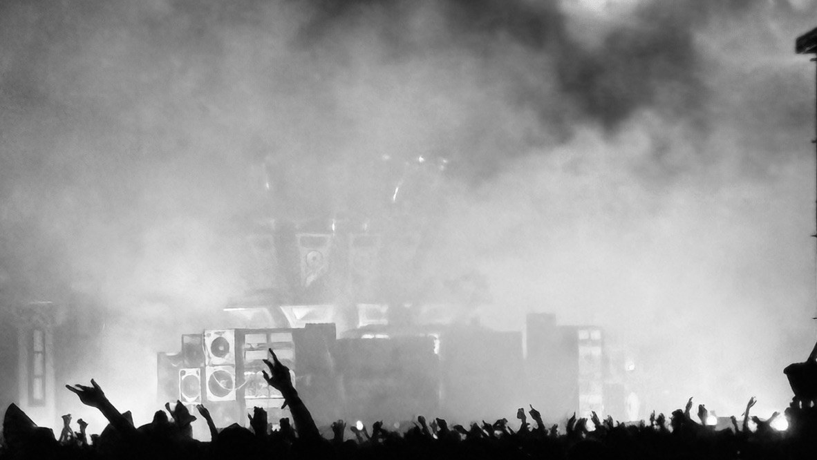 A concert crowd silhouetted beneath a smoke-filled stage